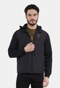 Giacca nera con zip e cappuccio, caratterizzata da una combinazione di texture lisce e a coste, un logo discreto sul petto e tasche laterali.