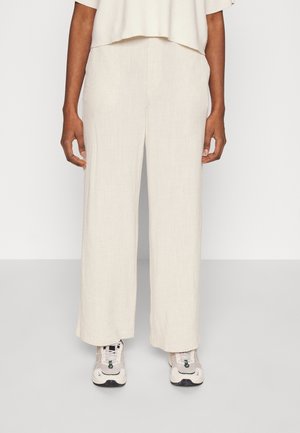 Pantalons en lin beige à jambes larges avec une finition texturée, présentant une coupe décontractée et associés à des baskets claires.