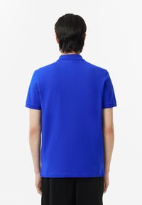 Blå polo skjorta gjord av ett mjukt, lättviktigt material. Har en klassisk krage och korta ärmar. Enkel design utan ytterligare mönster.