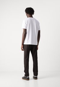 Hvit kortermet t-skjorte kombinert med svarte slim-fit bukser og svarte joggesko, med en glatt tekstur og minimalistisk design.
