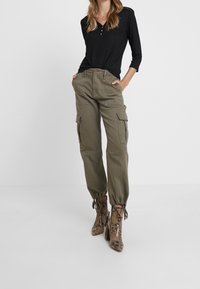 Olivgröna cargobyxor med elastiska muddar och sidofickor, kombinerat med en svart långärmad topp och mönstrade högklackade stövlar.