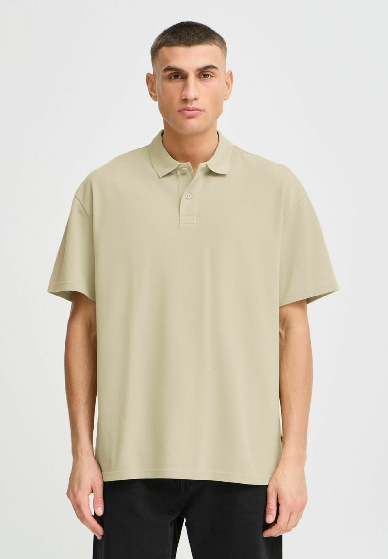 Polo skjorte i lys beige, laget av glatt stoff, med krage, korte ermer og tre knapper. Enkel, minimalistisk design.
