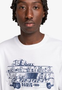 White cotton t-shirt featuring a blue illustration of a bus with passengers and luggage, labeled "ELEMENT PARIS" in bold lettering.
