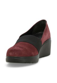 Scarpa con tacco in suede bordeaux con fascia elastica nera sopra la punta, punta arrotondata e suola spessa nera su sfondo bianco.