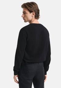 Schwarzer gestrickter Pullover mit strukturiertem Muster, mit rundem Halsausschnitt und gerippten Bündchen, kombiniert mit dunklen Hosen.