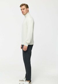 Pulover bej deschis cu guler înalt, cu mâneci lungi, asortat cu pantaloni gri închis și adidași albi. Textură netedă, design minimalist.