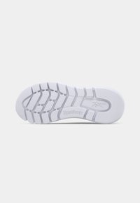 Semelle de chaussure de sport Reebok, en caoutchouc blanc avec des motifs de grip texturés, mettant en avant un logo bien visible. Bords lisses et arrondis avec un design flexible.