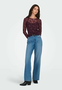 Top de encaje burdeos de manga larga con escote redondo, combinado con unos vaqueros de talle alto de pierna ancha en azul y botas de tobillo negras con tacón.