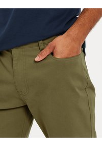 Pantalons en coton vert olive avec une coupe droite, dotés d'une poche latérale, de coutures visibles et d'une taille. Le tissu texturé est clairement visible.