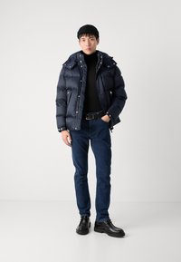 Marinblå puffjacka med texturerad yta, svart polotröja, mörkblå jeans och svarta skor, med en figursydd silhuett och avtagbar huva.