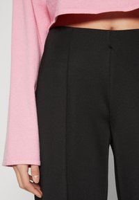 Black tailored pants paired with a pink cropped sweater, featuring a smooth texture and long sleeves. The pants have a clean, straight design.