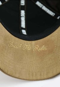 Khakifarbenes Cap mit schwarzem Innenfutter, das auf dem Schild "Break The Rules" in Gold gestickt hat. Strukturierter Stoff mit genähten Akzenten.