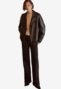 Chaqueta negra de cuero de doble botonadura con solapas amplias, combinada con un suéter beige de canalé y jeans negros de pierna recta. Diseño simple con acentos mínimos.