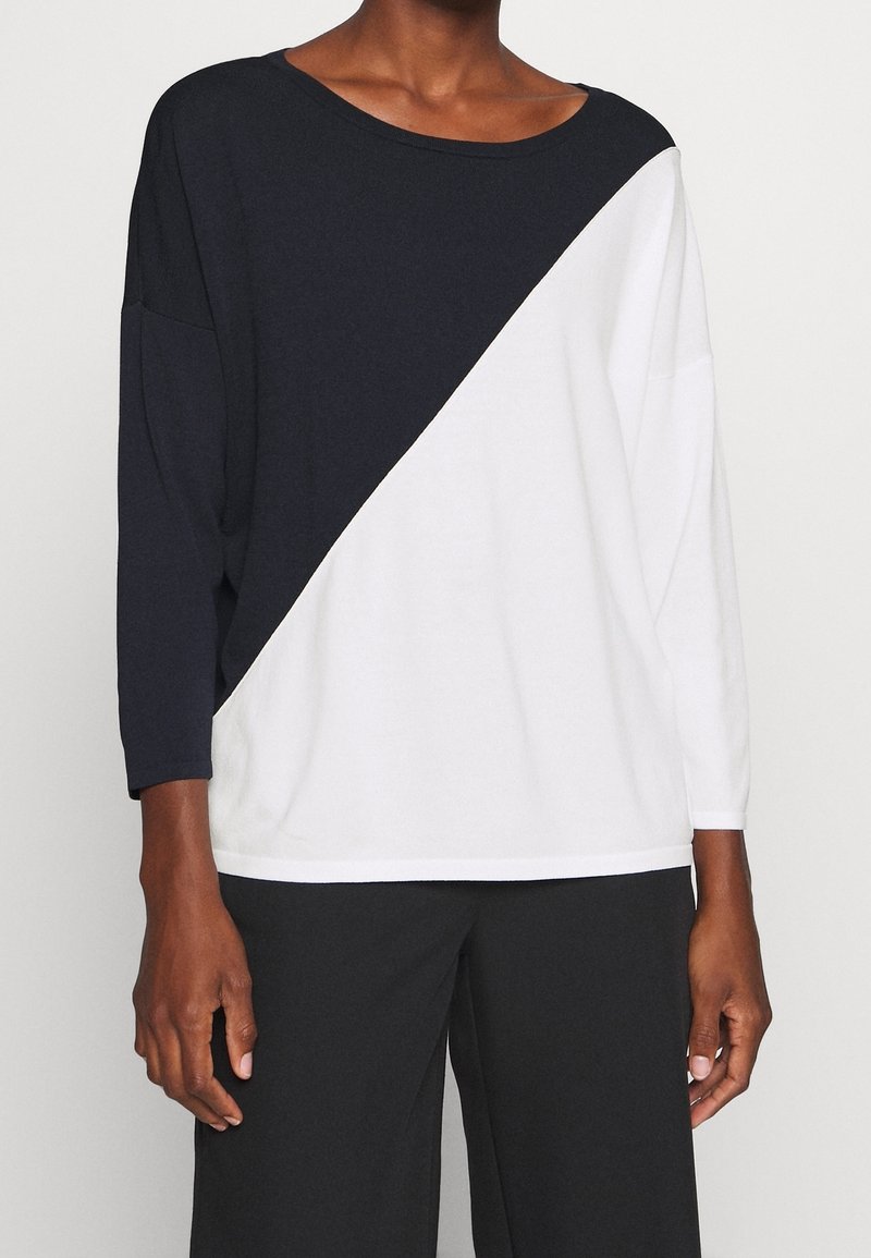 Camicia a blocchi di colore bianco e nero, realizzata in tessuto morbido, presenta un ampio scollo a barca e maniche lunghe con una vestibilità larga e una caduta rilassata.
