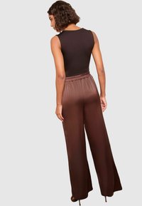 Zwarte mouwloze top gecombineerd met bruine satijnen wijde broek met elastische tailleband, van achteren gepresenteerd.