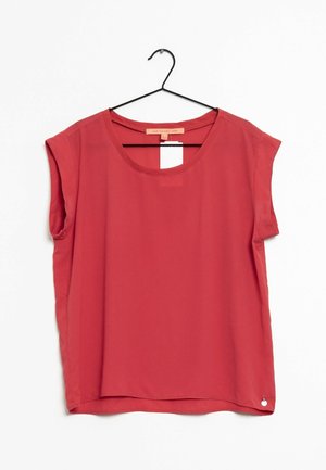 Rote ärmellose Bluse mit rundem Ausschnitt, die auf einem schwarzen Bügel vor weißem Hintergrund hängt.