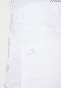 Pantaloni in cotone bianchi con una superficie liscia, dotati di una tasca posteriore e un dettaglio del logo a forma di cuore ricamato di colore azzurro.