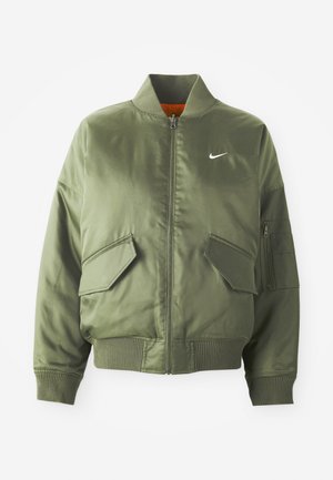 Olíva zöld bomber dzseki bordázott gallérral és mandzsettákkal, cipzáras záródással, két elülső zsebbel és egy oldalsó cipzáras zsebbel. A fehér Nike logó jellemzi.