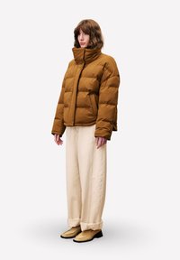 Bruin pufferjack met een hoge kraag en een opvallend quiltontwerp, gecombineerd met crèmekleurige broeken en beige schoenen. Eenvoudige, gestructureerde silhouet.