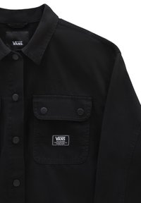 Schwarze Vans-Jacke mit Knopfdesign, zwei Fronttaschen mit Druckknopfverschluss und einem Etikett an der linken Tasche. Glatte Textur.