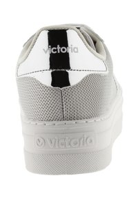 Zapatilla gris con parte superior de malla texturada y acento negro brillante. Presenta una suela blanca gruesa y un logo en el talón.