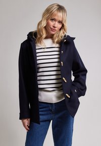 Marinblå ullkappa med huva, med guldpläterade knappar, sidofickor och en lätt figursydd passform över en randig topp och jeans.