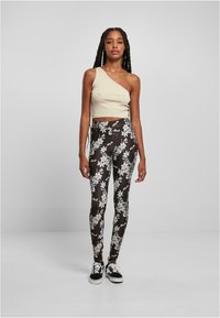 Ühe õla beez crop top, millele on sobitatud mustad lillemustriga retuusid, millel on valged lillemustrit. Mudel kannab musti ja valgeid tenisersch.