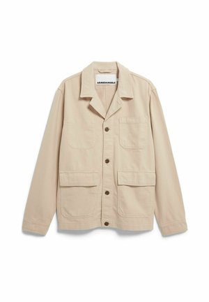 Giacca da lavoro beige in cotone con colletto, chiusura frontale con bottoni, due grandi tasche sul petto e una texture liscia. Etichetta del marchio: ARMEDANGELS.