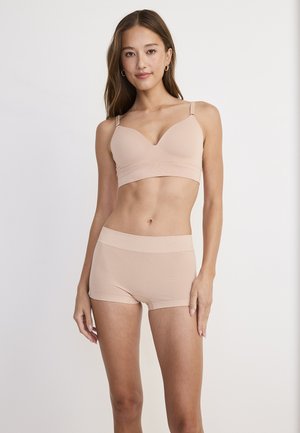 Skin-toned bralette with adjustable straps and smooth finish, paired with matching seamless boyshorts in similar material and color.