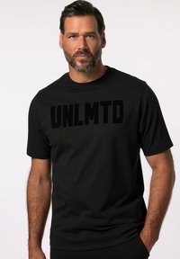 Camiseta negra de manga corta con un logo de terciopelo "UNLMTD" prominentemente exhibido en el pecho, fabricada con material de algodón suave.