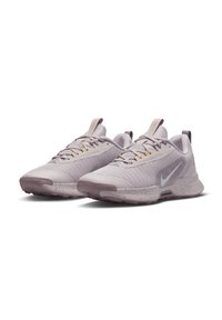 Lys lilla treningssko med teksturert overdel, hvit Nike-swoosh og prikkete grå såler. Har en trekkflekk og kontrasterende gule detaljer.