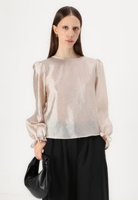 Lys rosa gjennomsiktig bluse med pufferm, laget av et blankt stoff. Kombinert med svarte bukser og holder en svart veske. Glatt tekstur og enkel design.