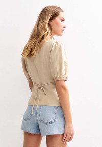 Beige linen top with puff sleeves and a tie at the waist, paired with light blue denim shorts. Textured fabric with a natural finish.