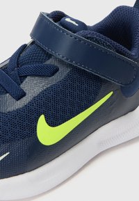 Marineblaues Mesh-Sportschuh mit Klettverschluss, neon grünen Akzenten und weißer Sohle. Verfügt über einen strukturierten Stoff und ein geschwungenes Design.