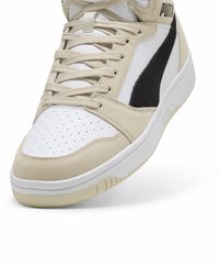 Baskets en suède beige et cuir blanc avec un accent noir, boîte à orteils perforée, lacets plats et semelle en caoutchouc blanc. Marque Puma à l'arrière.