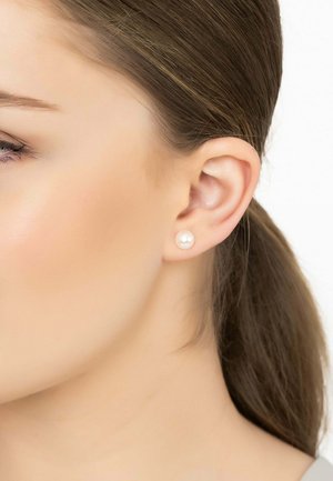 Pearl stud earrings featured on a woman's ear; they have a smooth, round shape, white color, and a glossy finish.