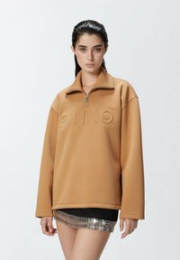 Felpa marrone con colletto zip e logo "PINKO" in rilievo. Presenta una vestibilità rilassata e una texture morbida, abbinata a una gonna con dettagli metallici.