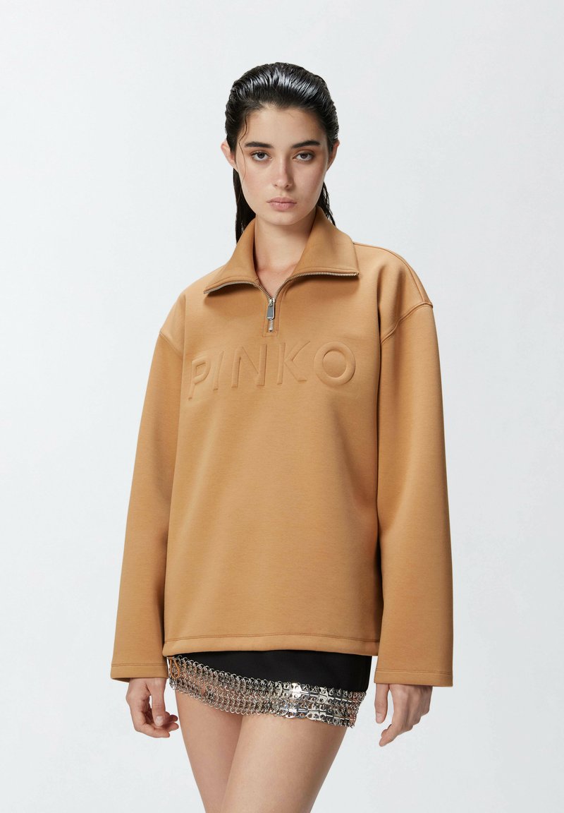 Felpa marrone con colletto zip e logo "PINKO" in rilievo. Presenta una vestibilità rilassata e una texture morbida, abbinata a una gonna con dettagli metallici.