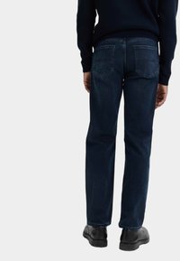 Mörkblå denimjeans med rak passform, synliga bakfickor och en ren midja, i kombination med svarta skor.