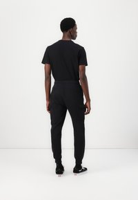 Black cotton T-shirt and jogger pants. Pants feature side pockets, elastic waist, and cuffs. Model facing away against a white background.