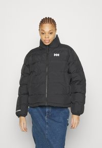 Black puffer jacket with zip closure, high collar, and ribbed cuffs. Features horizontal stitching and a white logo on the left chest.