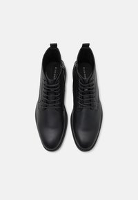 Botas de tobillo de cuero negro con un diseño elegante, que cuentan con cierre de cordones y cremalleras laterales, textura suave y punta redondeada.
