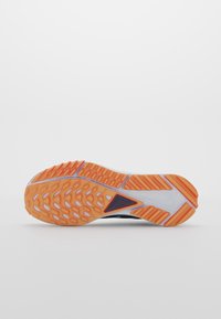 Semelle en caoutchouc orange et blanche à motifs d'une chaussure de sport, avec des sections de grip texturé sur fond blanc.