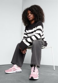 Scarpe Nike rosa con accenti bianchi, suola nera e ammortizzazione ad aria. Maglione a righe bianche e nere, pantaloni larghi grigi.