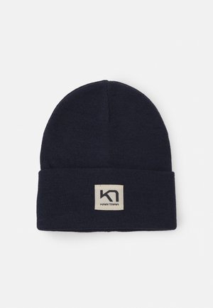 Marinblå stickad mössa med uppvikt kant och en fyrkantig etikett med en svart logotyp. Tillverkad av mjukt tyg med en slät yta.