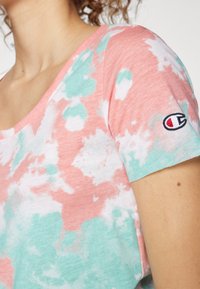 Camiseta de manga corta con un patrón de tie-dye en rosa y menta, fabricada con tela suave. Incluye un parche de logotipo en la manga izquierda.