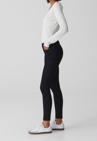 Jeans ajustados negros con bolsillos, combinados con una camiseta blanca de manga larga y zapatillas blancas. Tejido suave con un diseño ceñido.