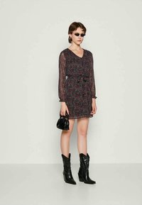 Vestido preto com estampado floral, mangas longas transparentes, decote em V e laço na cintura. Combinado com botas pretas de estilo western e uma pequena bolsa preta.