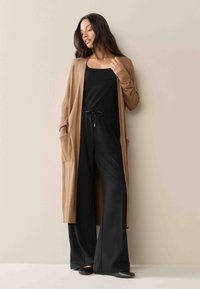 Long brown cardigan with side pockets, black top, wide-leg black pants, and black flats. Smooth texture and simple design.
