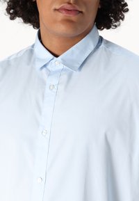 Camicia azzurra chiaro con bottoni, colletto classico, realizzata in tessuto liscio, con bottoni bianchi sul davanti e vestibilità rilassata.